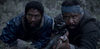 Movie still from “Black Summer” (2019), created by John Hyams – Two men laying on the ground with a rifle; Close Up shot, Low angle