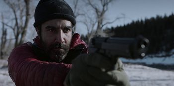 Movie still from “Black Summer” (2019), created by John Hyams – A man with a beard is holding a gun; Close Up shot, Over the shoulder angle