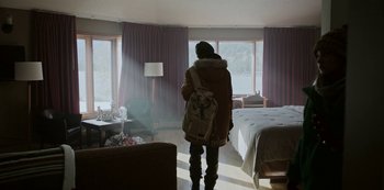 Movie still from “Black Summer” (2019), created by John Hyams – A person standing in a room with a backpack; Wide shot, High angle