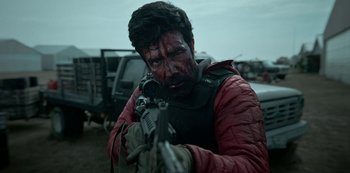 Movie still from “Black Summer” (2019), created by John Hyams – A man in a red jacket is holding a gun; Medium shot, Over the shoulder angle