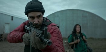 Movie still from “Black Summer” (2019), created by John Hyams – A man holding a gun while standing next to a woman; Medium shot, Over the shoulder angle