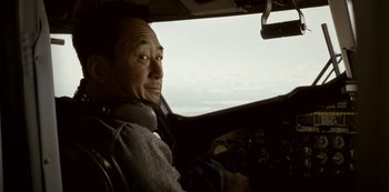 Movie still from “Black Summer” (2019), created by John Hyams – A man with headphones sitting in the cockpit of an airplane; Medium shot, Low angle