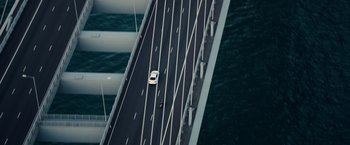 Movie still from “Blackhat” (2015), directed by Michael Mann – An aerial view of a car driving on a bridge over a body of water; Extreme Wide shot, Overhead angle