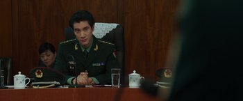 Movie still from “Blackhat” (2015), directed by Michael Mann – A man sitting at a table in a military uniform; Medium shot, Over the shoulder angle