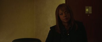 Movie still from “Blackhat” (2015), directed by Michael Mann – A woman sitting in front of a chair in front of a wall; Close Up shot, Over the shoulder angle