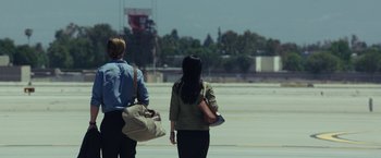 Movie still from “Blackhat” (2015), directed by Michael Mann – A man and a woman walking across an airport tarmac; Wide shot, Over the shoulder angle