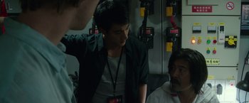 Movie still from “Blackhat” (2015), directed by Michael Mann – A man standing in front of two other men; Medium shot, Over the shoulder angle