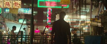 Movie still from “Blackhat” (2015), directed by Michael Mann – A man standing in front of a building at night; Wide shot, Over the shoulder angle