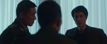 Movie still from “Blackhat” (2015), directed by Michael Mann – A group of people sitting in a room talking to each other; Medium shot, Over the shoulder angle