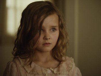 Movie still from “Blonde” (2022), directed by Andrew Dominik – A little girl with long brown hair wearing a pink dress; Close Up shot, Over the shoulder angle