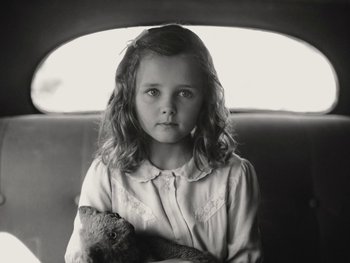 Movie still from “Blonde” (2022), directed by Andrew Dominik – A little girl sitting in the back of a car holding a stuffed animal; Close Up shot, High angle