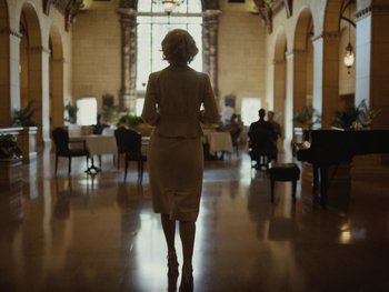 Movie still from “Blonde” (2022), directed by Andrew Dominik – A woman in a white dress is walking in a room; Wide shot, Over the shoulder angle
