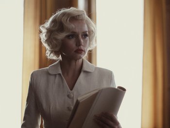 Movie still from “Blonde” (2022), directed by Andrew Dominik – A woman with blonde hair holding a book in front of a window; Medium shot, Low angle