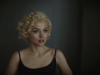 Movie still from “Blonde” (2022), directed by Andrew Dominik – A woman with blonde curly hair wearing a black top; Close Up shot, Over the shoulder angle
