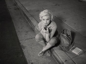 Movie still from “Blonde” (2022), directed by Andrew Dominik – A black and white photo of a woman sitting on the sidewalk; Medium shot, High angle