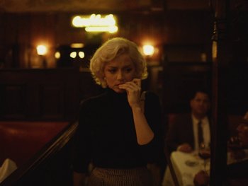 Movie still from “Blonde” (2022), directed by Andrew Dominik – A woman in a black shirt and a man in a black suit; Medium shot, Low angle