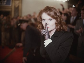 Movie still from “Blonde” (2022), directed by Andrew Dominik – A woman in a black jacket and black gloves holding her finger to her mouth; Close Up shot, Low angle