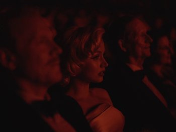 Movie still from “Blonde” (2022), directed by Andrew Dominik – A group of people sitting in a dark room; Medium shot, Over the shoulder angle