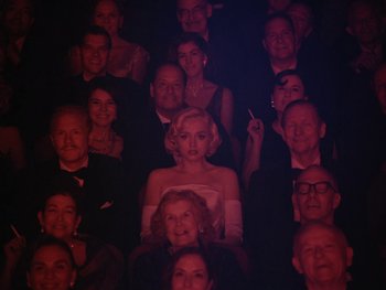 Movie still from “Blonde” (2022), directed by Andrew Dominik – A group of people that are sitting in a dark room; Wide shot, High angle