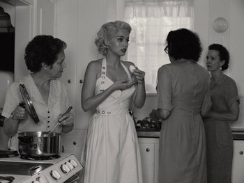 Movie still from “Blonde” (2022), directed by Andrew Dominik – A woman in a white dress in a kitchen with three other women; Medium shot, High angle