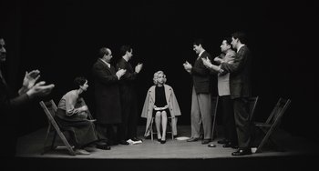 Movie still from “Blonde” (2022), directed by Andrew Dominik – A group of people standing around a woman sitting on a chair; Wide shot, High angle