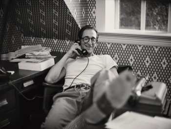 Movie still from “Blonde” (2022), directed by Andrew Dominik – A man sitting on a chair while talking on a phone; Medium shot, High angle