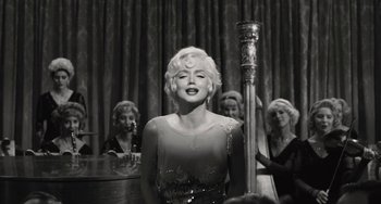 Movie still from “Blonde” (2022), directed by Andrew Dominik – A woman standing next to a microphone in front of a group of women; Medium shot, Over the shoulder angle