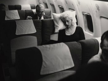 Movie still from “Blonde” (2022), directed by Andrew Dominik – An older man and a woman sitting on a seat on an airplane; Medium shot, High angle