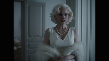 Movie still from “Blonde” (2022), directed by Andrew Dominik – A woman in a white dress and a white fur stole; Medium shot, Over the shoulder angle