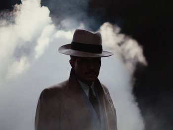 Movie still from “Blonde” (2022), directed by Andrew Dominik – A man wearing a hat and a suit standing in front of smoke; Medium shot, Low angle