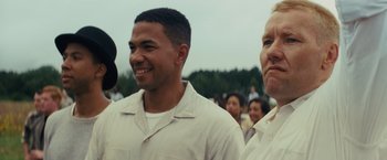 Movie still from “Loving” (2016), directed by Jeff Nichols – A man standing next to another man in front of a group of people; Medium shot, Over the shoulder angle