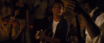 Movie still from “Loving” (2016), directed by Jeff Nichols – A man holding a guitar in front of a group of people; Medium shot, Low angle