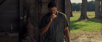 Movie still from “Loving” (2016), directed by Jeff Nichols – A man eating a piece of food while standing in front of a building; Medium shot, Low angle