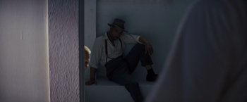 Movie still from “Loving” (2016), directed by Jeff Nichols – A man sitting on the ground wearing a hat; Medium shot, Low angle