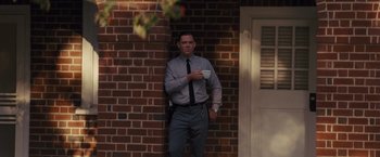 Movie still from “Loving” (2016), directed by Jeff Nichols – A man standing in front of a brick wall holding a coffee cup; Medium shot, Low angle