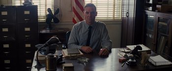 Movie still from “Loving” (2016), directed by Jeff Nichols – A man sitting at a table in front of an american flag; Medium shot, Low angle