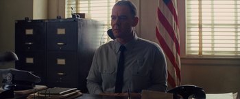 Movie still from “Loving” (2016), directed by Jeff Nichols – A man sitting at a desk in front of an american flag; Medium shot, Low angle