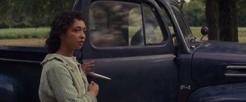 Movie still from “Loving” (2016), directed by Jeff Nichols – A woman holding a cigarette in her left hand while standing next to a car; Medium shot, Over the shoulder angle