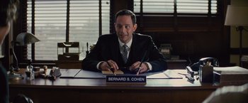 Movie still from “Loving” (2016), directed by Jeff Nichols – A man sitting at a desk in front of a sign that reads " bernard s; Medium shot, Over the shoulder angle