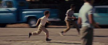 Movie still from “Loving” (2016), directed by Jeff Nichols – Two young boys running on the street in front of a car; Wide shot, High angle