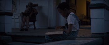 Movie still from “Loving” (2016), directed by Jeff Nichols – A boy sitting on the floor reading a book; Medium shot, High angle