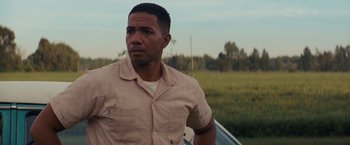 Movie still from “Loving” (2016), directed by Jeff Nichols – A man standing next to a car in a grassy field; Close Up shot, Low angle