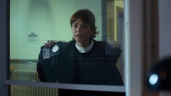 Movie still from “Marcella” (2016), created by Hans Rosenfeldt – A woman holding up a police badge in front of a window; Medium shot, Over the shoulder angle