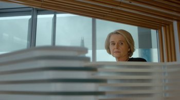 Movie still from “Marcella” (2016), created by Hans Rosenfeldt – An older woman looking out of a window at stacks; Medium shot, Low angle