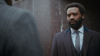 Movie still from “Marcella” (2016), created by Hans Rosenfeldt – A man in a suit standing next to a brick wall; Close Up shot, Over the shoulder angle