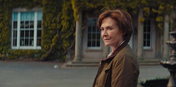 Movie still from “Marcella” (2016), created by Hans Rosenfeldt – A woman standing in front of a building with trees in the background; Close Up shot, Over the shoulder angle