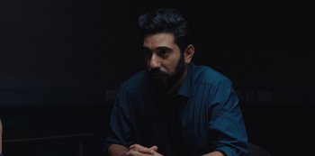 Movie still from “Marcella” (2016), created by Hans Rosenfeldt – A man with a beard is sitting in a dark room; Medium shot, Over the shoulder angle