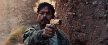 A man holding a gun while standing next to a tree