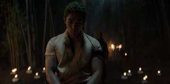 Movie still from “One Piece” (2023), directed by Marc Jobst – A man with green hair is standing in the dark; Medium shot, Over the shoulder angle