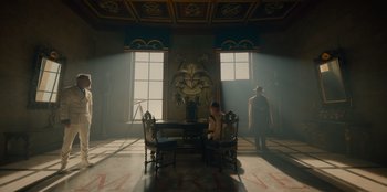 Movie still from “One Piece” (2023), directed by Marc Jobst – A man sitting at a table in a room with two large windows; Wide shot, Low angle
